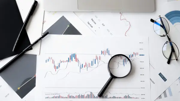 Financial charts with a magnifying glass and glasses on a desk
