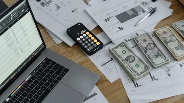 حاسوب محمول وآلة حاسبة وأوراق نقدية ومستندات مالية على مكتب
