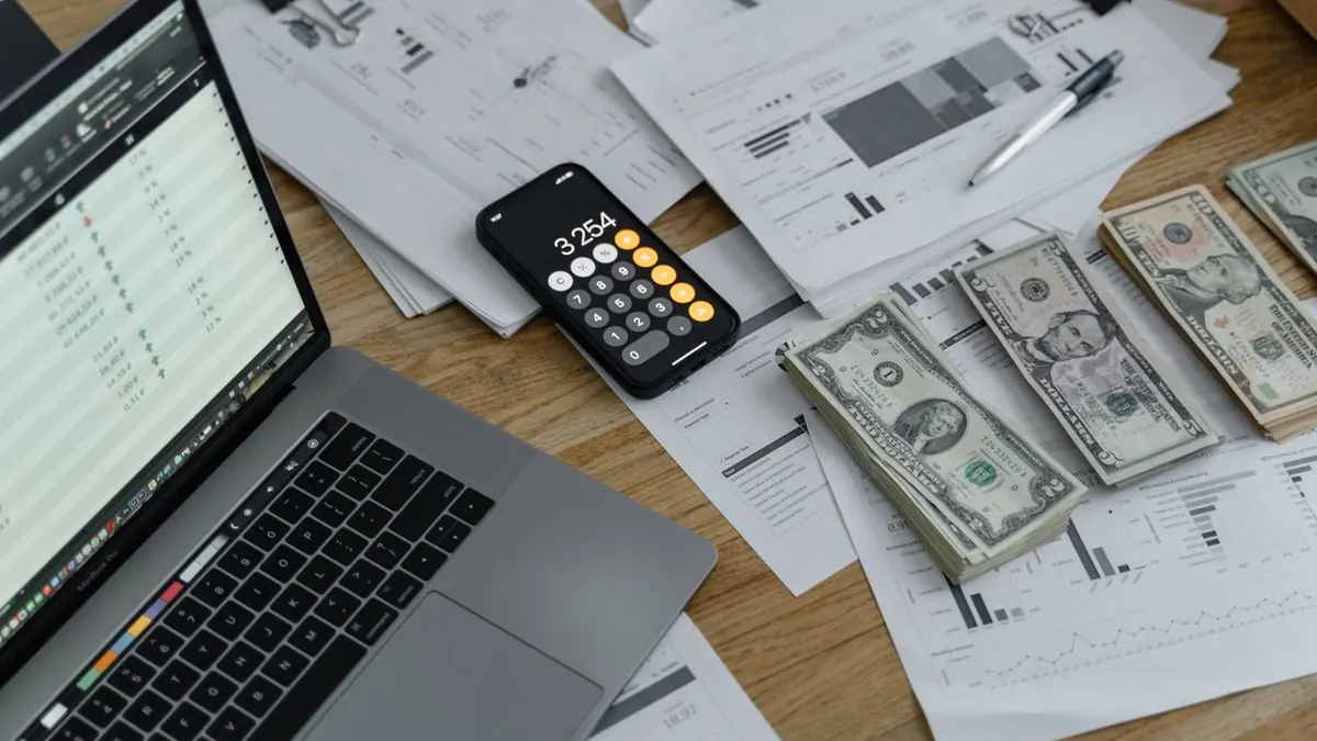 حاسوب محمول وآلة حاسبة وأوراق نقدية ومستندات مالية على مكتب