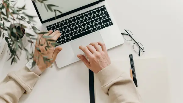 Hands typing on a laptop at a clean white desk