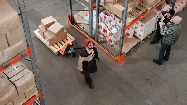 Workers moving boxes in a warehouse with tall shelving