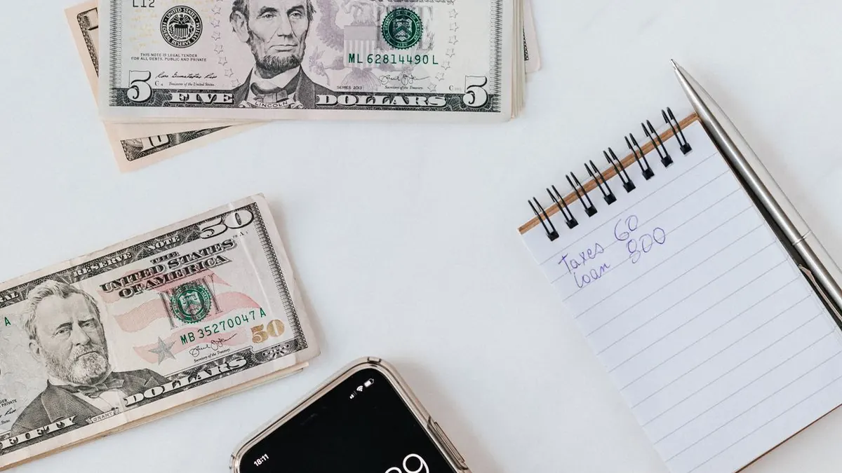 Hand using a calculator next to banknotes and a notepad