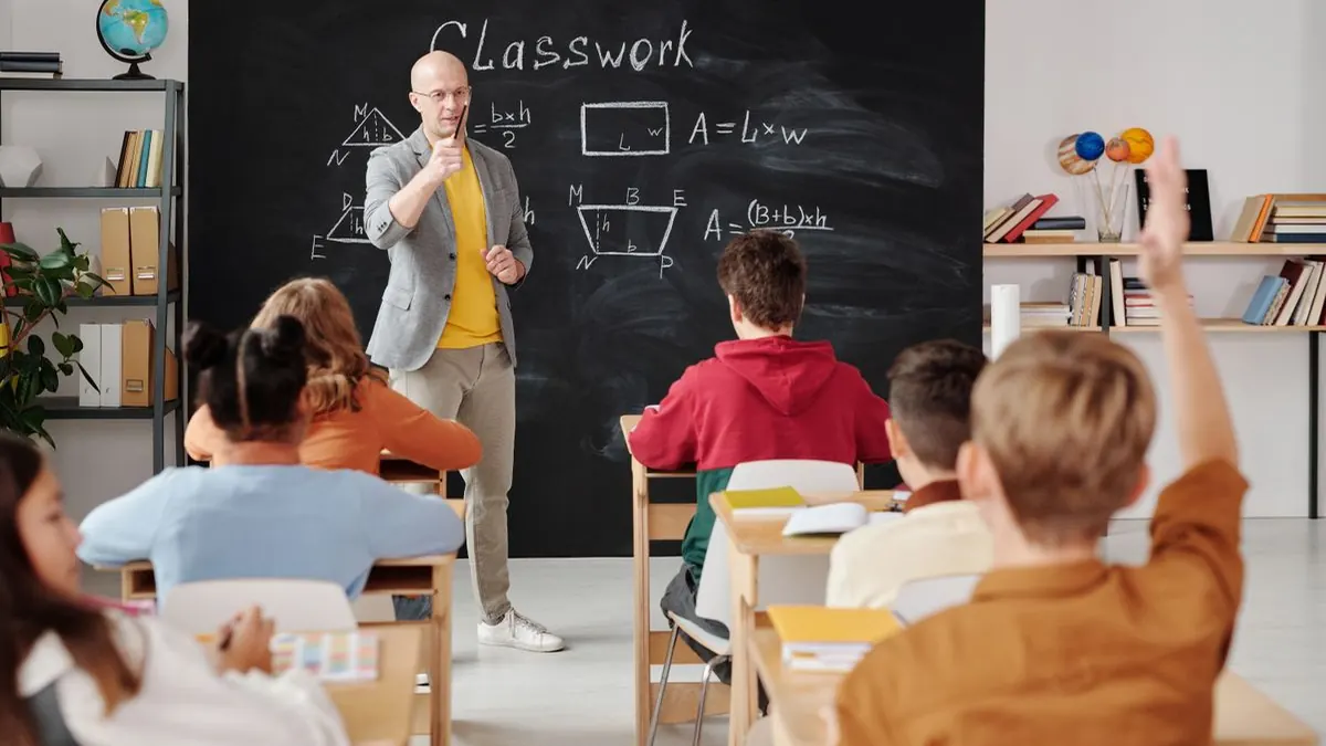 Teacher in front of a blackboard with students raising hands